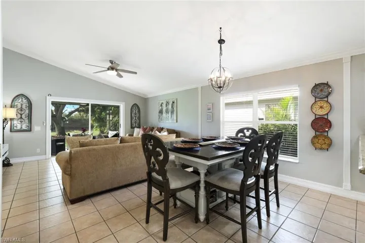 Dining area featuring light tile patterned floors, lofted ceiling, ceiling fan with notable chandelier, baseboards, and ornamental molding