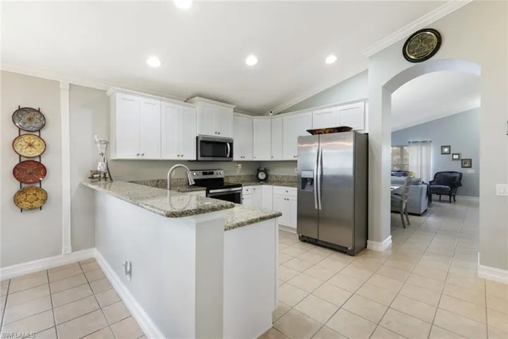 Kitchen with light tile patterned floors, arched walkways, white cabinets, a peninsula, and stainless steel appliances