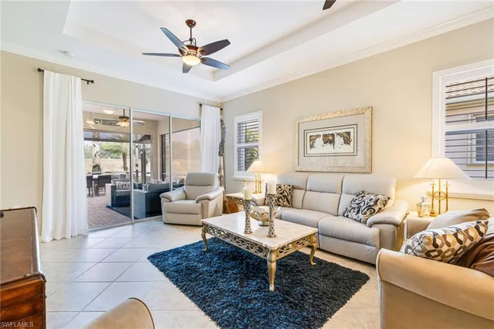 Living room with a tray ceiling, light tile patterned floors, ornamental molding, healthy amount of natural light, and ceiling fan