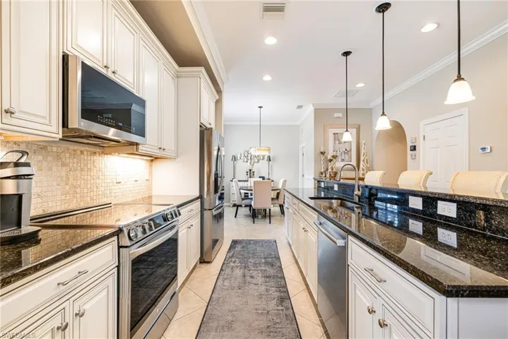 Kitchen featuring stainless steel appliances, ornamental molding, dark stone counters, decorative backsplash, and pendant lighting