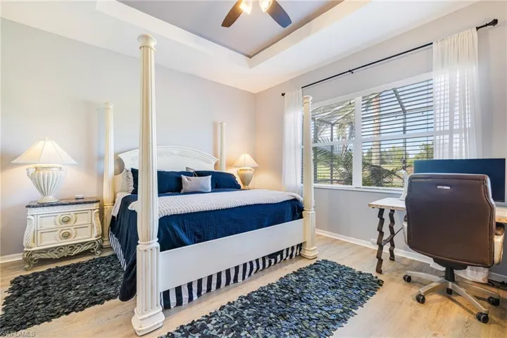 Bedroom with a raised ceiling, light wood-style floors, a desk, and ceiling fan