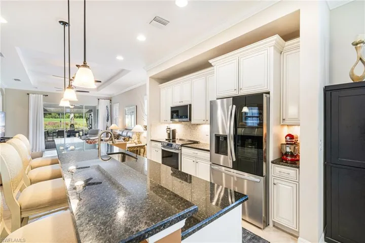 Kitchen with crown molding, hanging light fixtures, appliances with stainless steel finishes, a breakfast bar, and a raised ceiling