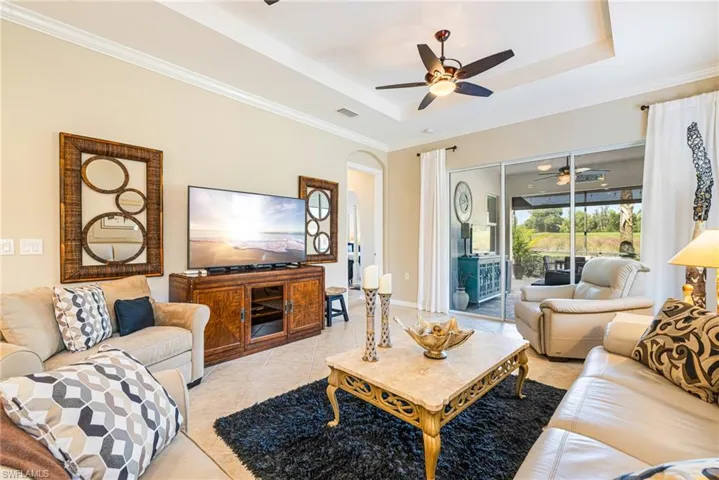 Living room featuring a tray ceiling, light tile patterned flooring, crown molding, a ceiling fan, and arched walkways