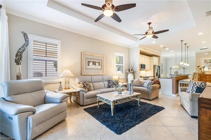 Living area featuring light tile patterned floors, ornamental molding, a ceiling fan, a tray ceiling, and recessed lighting