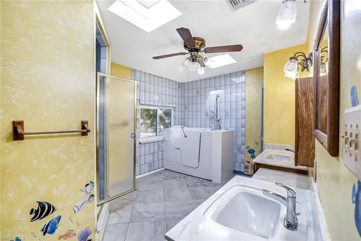 Full bathroom featuring vanity, a bath, a stall shower, ceiling fan, and a skylight