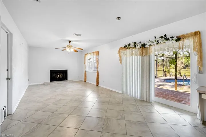 Unfurnished living room featuring a fireplace with raised hearth, a ceiling fan, and light tile patterned floors