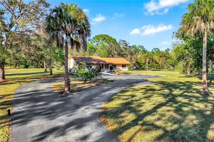 View of front of house with asphalt driveway, a front yard, and view of scattered trees