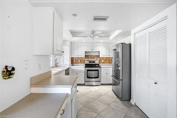 Kitchen featuring stainless steel appliances, a tray ceiling, white cabinets, light countertops, and ceiling fan