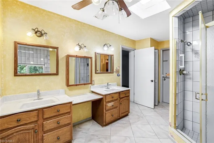 Full bath with double vanity, ceiling fan, a shower stall, and a skylight
