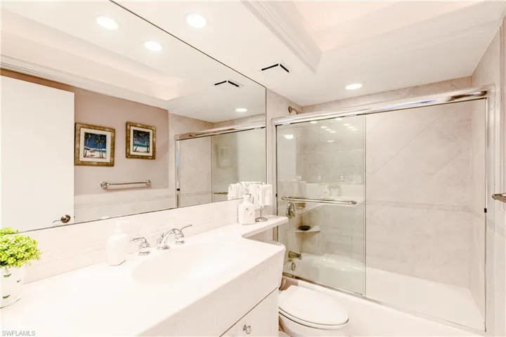 Full bathroom featuring vanity, a raised ceiling, bath / shower combo with glass door, toilet, and ornamental molding