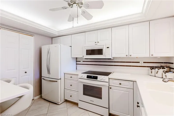 Kitchen featuring white appliances, backsplash, a tray ceiling, white cabinetry, and ceiling fan