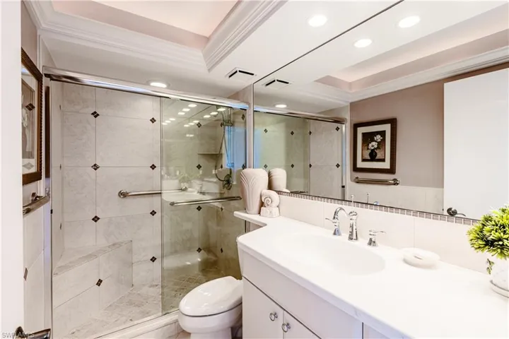 Bathroom featuring a shower with shower door, toilet, a raised ceiling, and vanity
