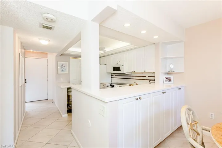 Kitchen featuring white cabinets, white appliances, a textured ceiling, kitchen peninsula, and light tile patterned flooring
