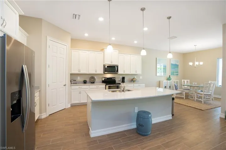 Kitchen with appliances with stainless steel finishes, hanging light fixtures, wood tiled floors, white cabinets, and recessed lighting