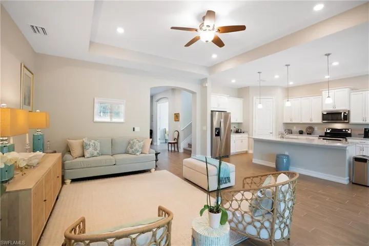 Living area featuring arched walkways, light wood-style flooring, ceiling fan, recessed lighting, and a tray ceiling