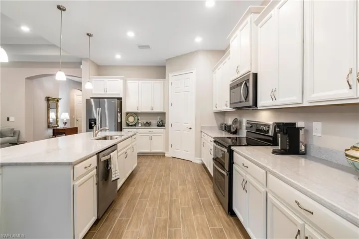 Kitchen with stainless steel appliances, hanging light fixtures, white cabinets, light stone countertops, and recessed lighting
