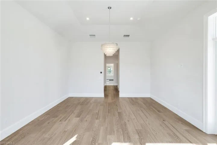 Unfurnished room with hanging lights, light wood-style floors, and lofted ceiling