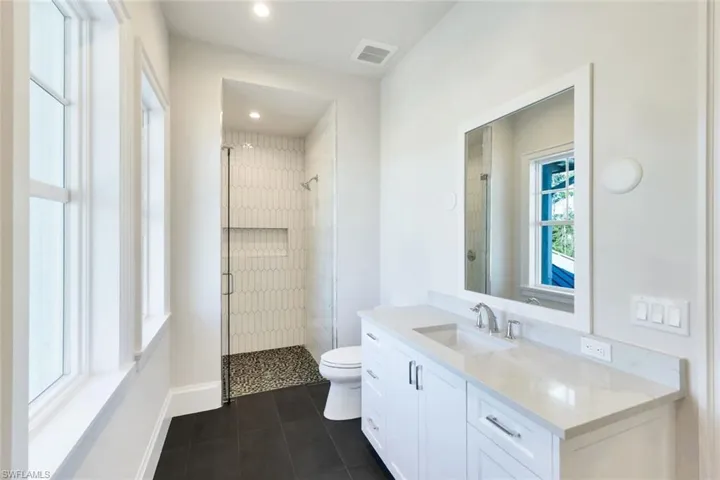 Bathroom with a shower stall, vanity, dark tile patterned flooring, and recessed lighting