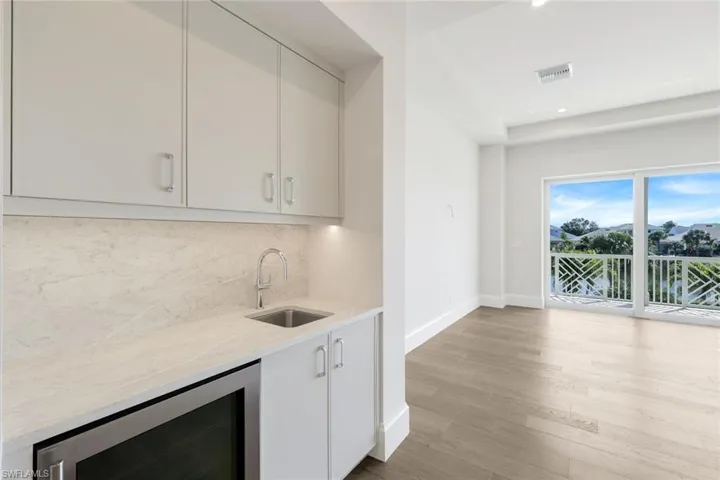 Indoor wet bar with beverage cooler, light stone counters, light wood-type flooring, recessed lighting, and tasteful backsplash