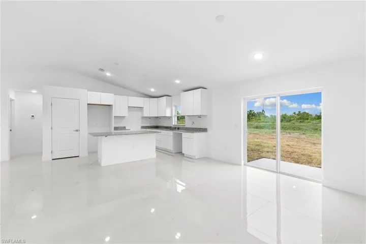 Kitchen featuring lofted ceiling, a center island, white cabinets, recessed lighting, and baseboards
