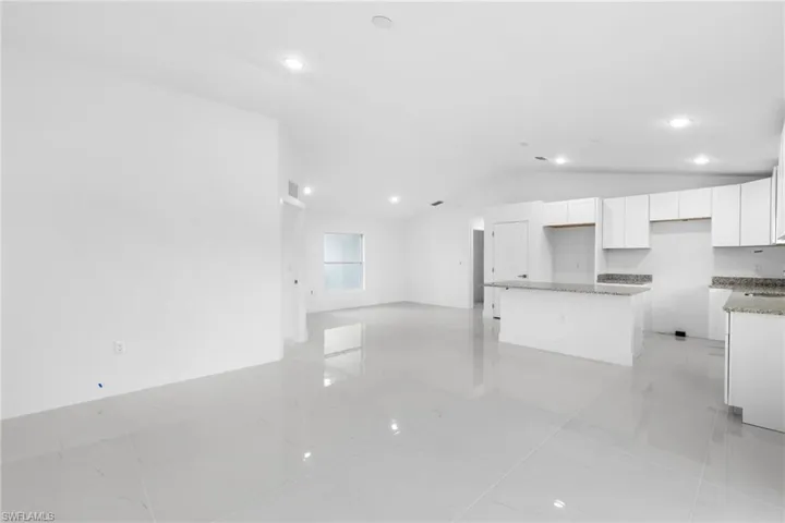 Unfurnished living room featuring vaulted ceiling, recessed lighting, and baseboards