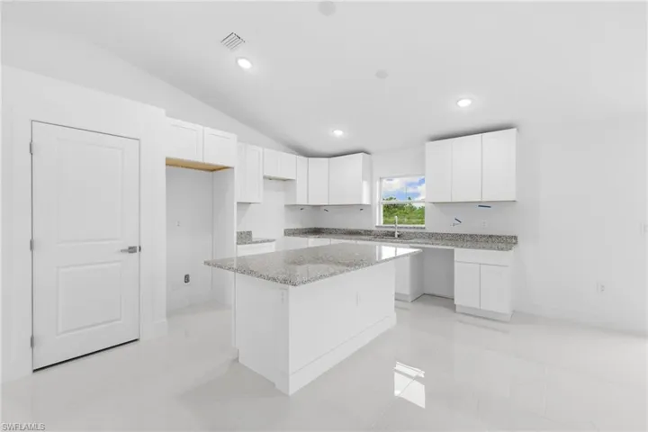 Kitchen with vaulted ceiling, a center island, white cabinetry, light stone countertops, and recessed lighting