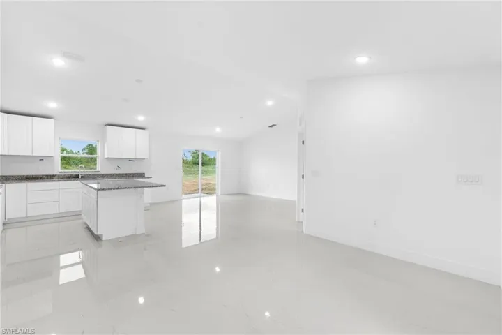 Kitchen with recessed lighting, open floor plan, white cabinetry, a kitchen island, and baseboards