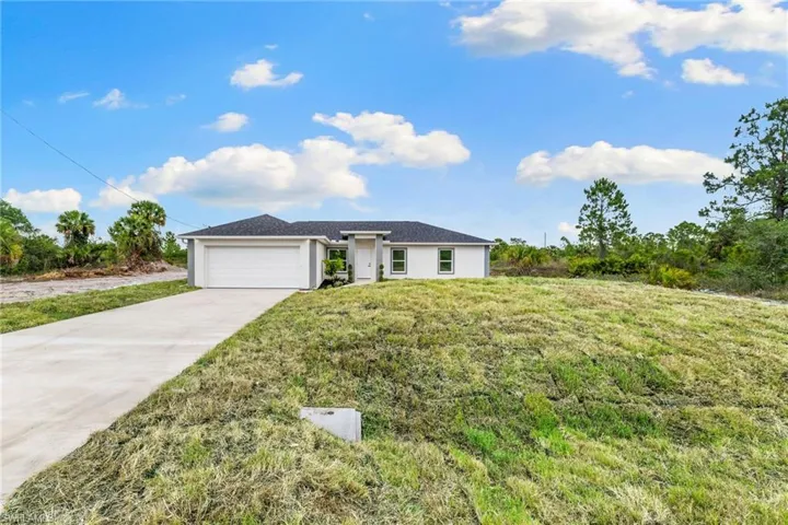 Ranch-style house with an attached garage, driveway, a front yard, and stucco siding