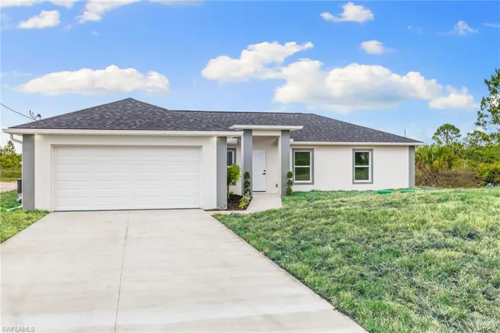 View of front facade with stucco siding, driveway, a front yard, a garage, and roof with shingles