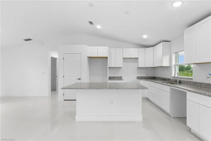 Kitchen featuring a sink, a kitchen island, lofted ceiling, light stone counters, and white cabinetry