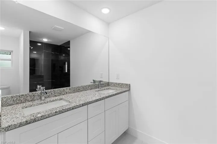 Full bathroom with a shower stall, double vanity, baseboards, recessed lighting, and toilet
