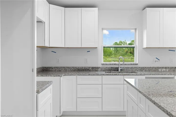 Kitchen featuring a sink, white cabinets, and light stone counters