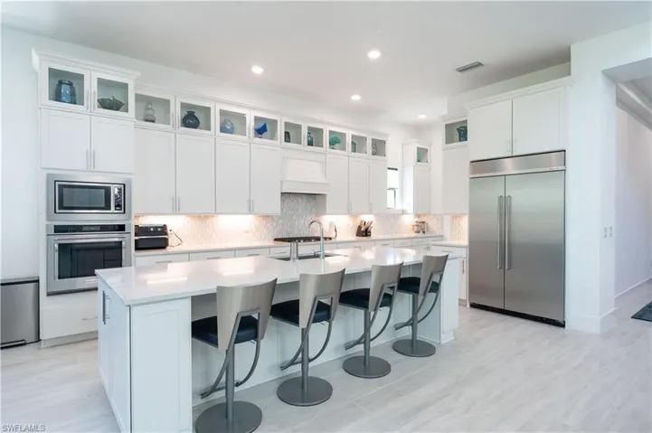 Kitchen with an island with sink, visible vents, built in appliances, light countertops, and custom range hood