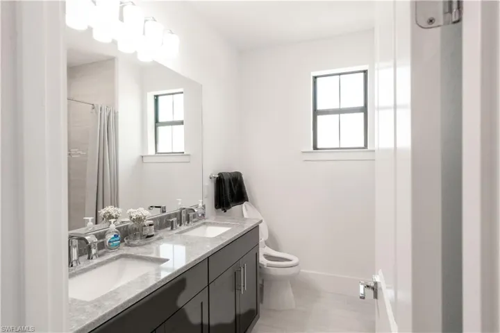 Bathroom featuring a sink, double vanity, toilet, and baseboards