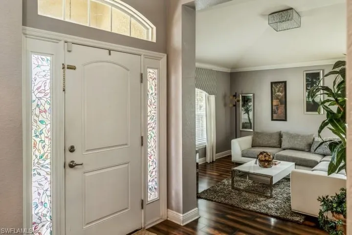 Entryway with dark wood-type flooring, crown molding, and vaulted ceiling
