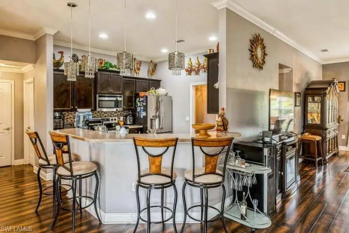 Kitchen featuring hanging light fixtures, dark brown cabinetry, appliances with stainless steel finishes, decorative backsplash, and a kitchen breakfast bar