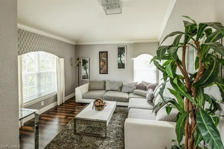 Living room with vaulted ceiling, dark wood-style flooring, and ornamental molding