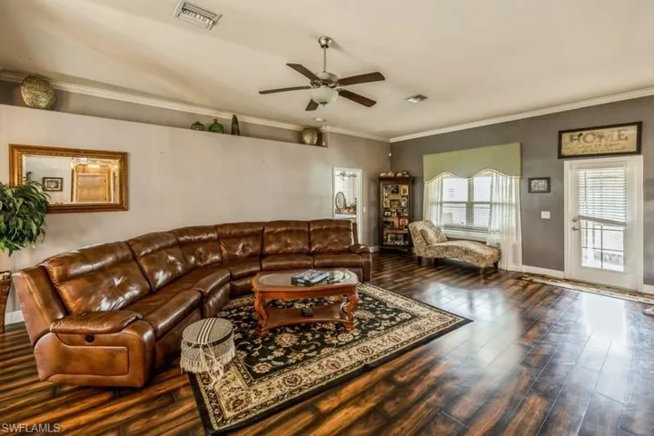 Living room with ornamental molding, ceiling fan, and dark wood finished floors