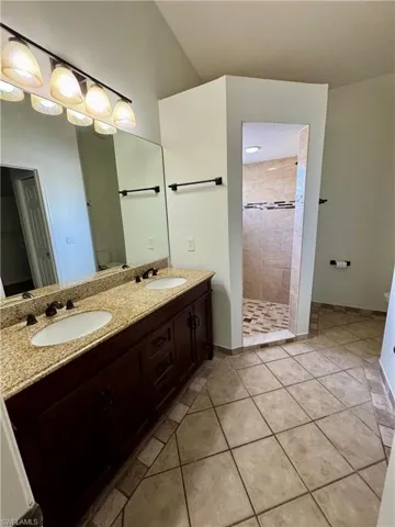 Primary Bathroom with double sinks, tiled shower, and large walk-in closet