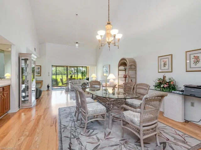 Dining area with high vaulted ceiling, light wood finished floors, a chandelier, and ceiling fan