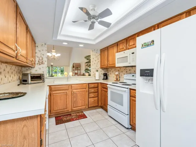 Kitchen with white appliances, brown cabinetry, light countertops, and light tile patterned flooring