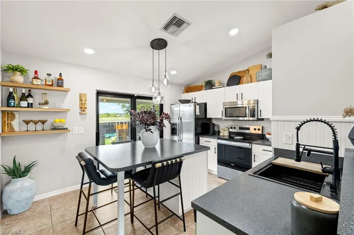 Kitchen featuring appliances with stainless steel finishes, dark countertops, white cabinetry, lofted ceiling, and pendant lighting