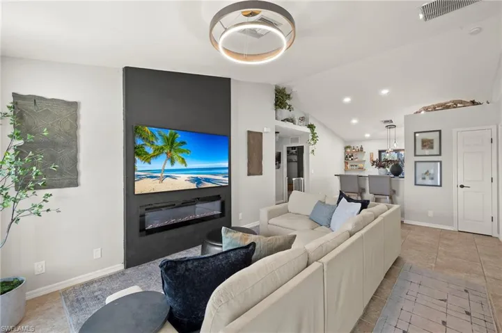Living area featuring a glass covered fireplace, vaulted ceiling, light tile patterned floors, and recessed lighting