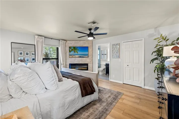 Bedroom with a large fireplace, multiple windows, light wood-type flooring, and a ceiling fan