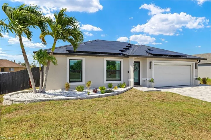 View of front of home featuring stucco siding, a garage, driveway, and solar panels