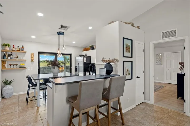 Kitchen featuring stainless steel fridge, a kitchen bar, dark countertops, a peninsula, and decorative light fixtures
