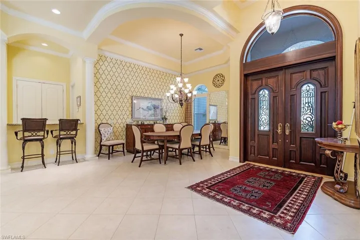 Foyer entrance and formal dining room, featuring crown molding, an inviting chandelier, neutral  flooring