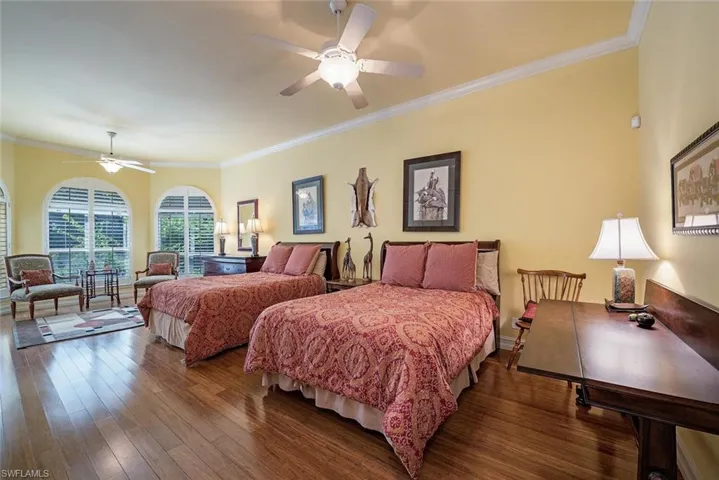Expansive guest bedroom featuring crown molding, dark wood-type flooring, and ceiling fan