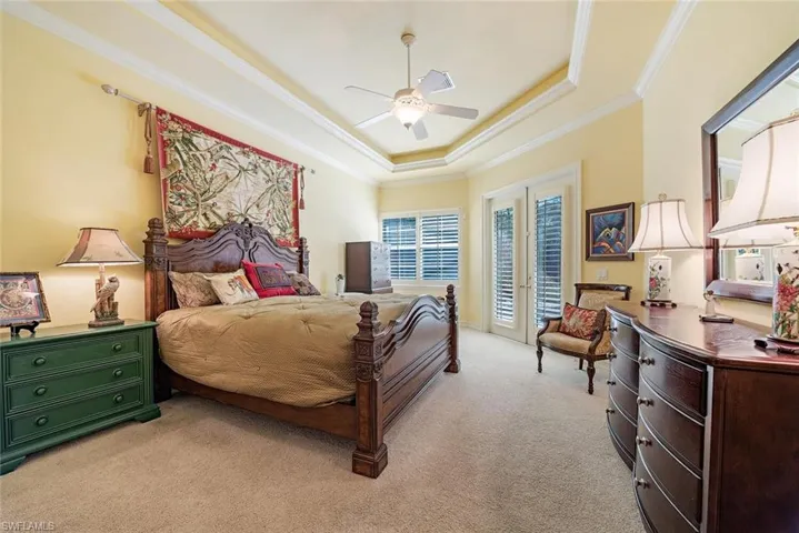 Expansive primary Bedroom with crown molding, light colored carpet, a tray ceiling, access to lanai