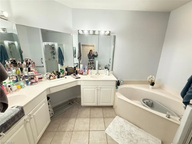 Full bath with double vanity, light tile patterned flooring, a garden tub, and a shower stall